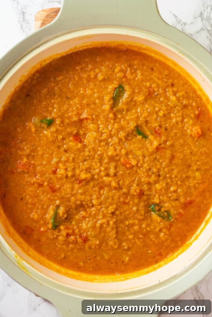 Combining Cooked Lentils with Tadka A large pan filled with the vibrant red lentil dal, showing the creamy texture and rich color, after the cooked lentils have been combined with the aromatic spice and tomato mixture and simmered together.