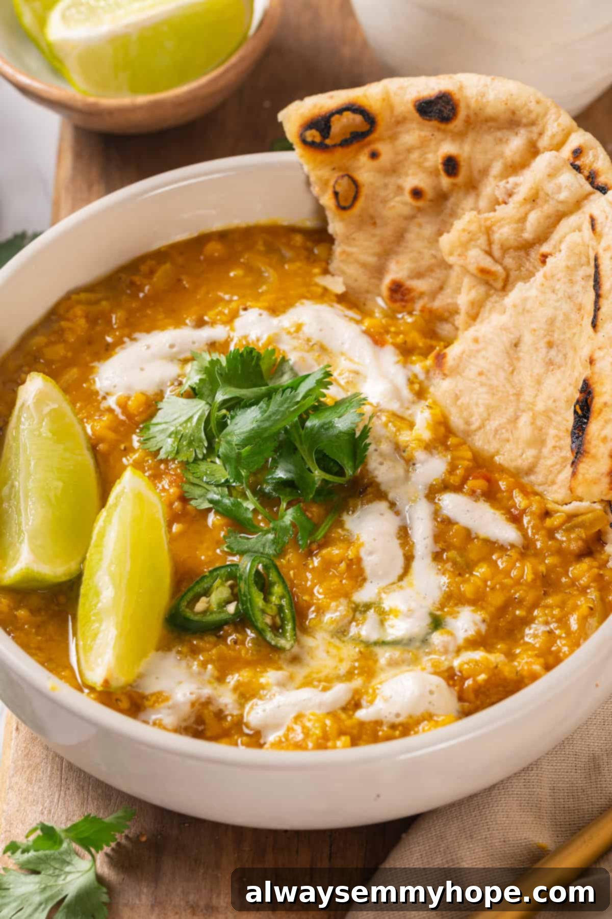 Red Lentil Dal Served with Naan and Lime A generously sized bowl of rich, creamy red lentil dal, topped with fresh green cilantro, and served alongside fluffy vegan naan bread and bright lime wedges.