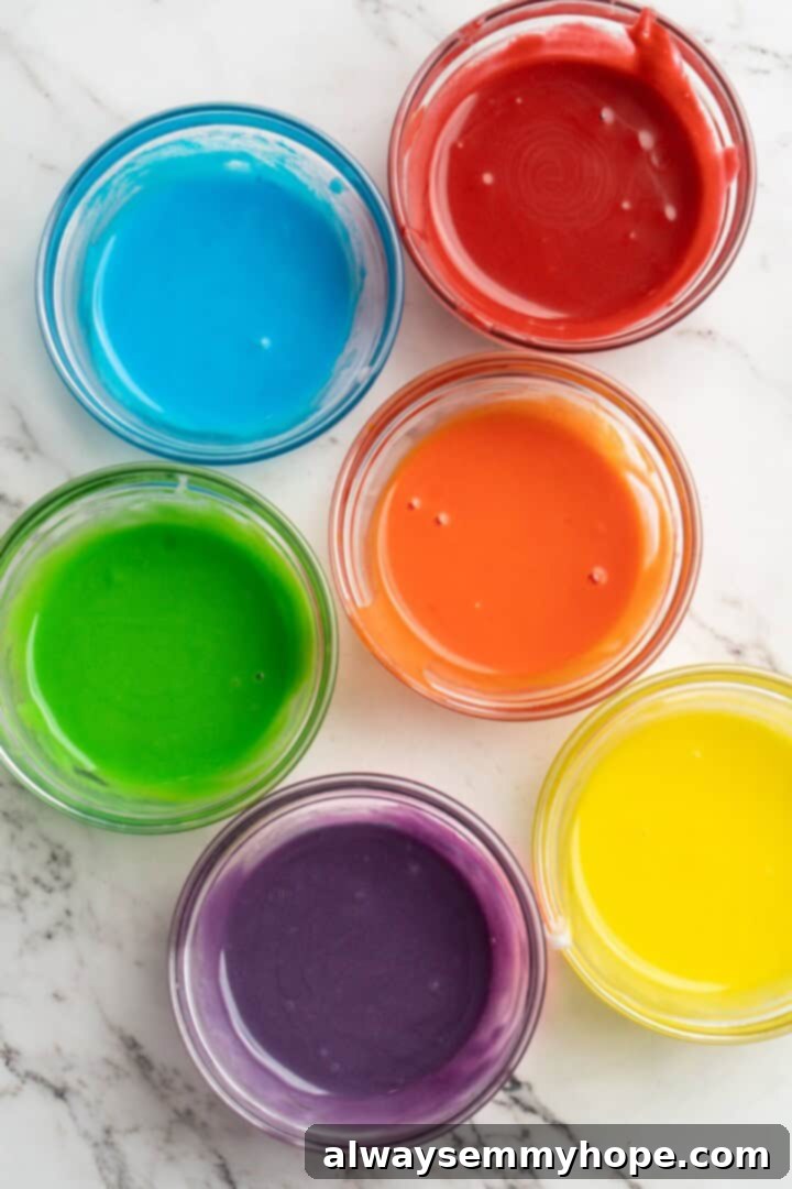 Several small bowls containing white icing, each tinted with a different vibrant food coloring, ready for piping.