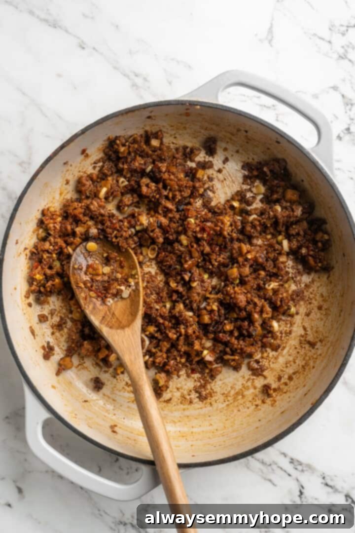 Adding aromatics to the vegan Mapo Tofu base Aromatics like ginger, garlic, and scallion whites cooking with the vegan meat and mushrooms in a pan, becoming fragrant.