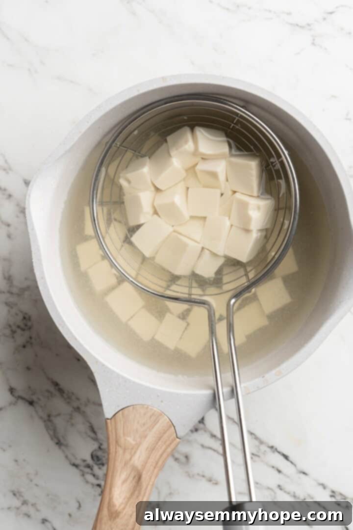 Boiling silken tofu in salted water for tenderness Cubed silken tofu gently boiling in a pot of salted water, preparing it for the Mapo Tofu sauce.