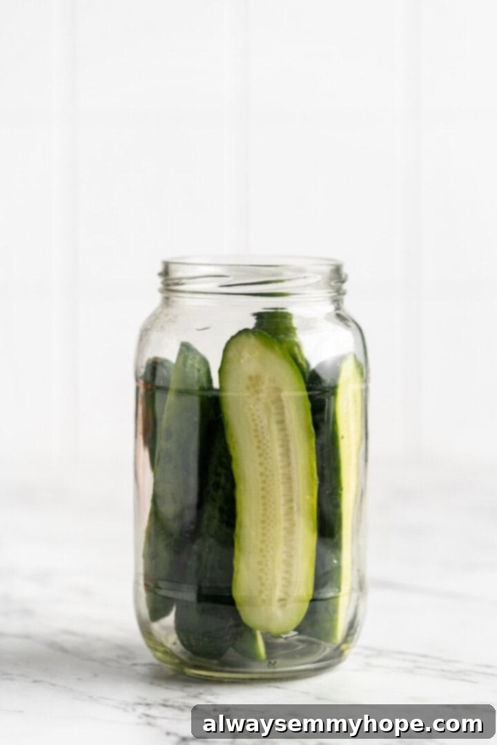 Clean glass jar filled with freshly sliced cucumbers, ready for pickling.