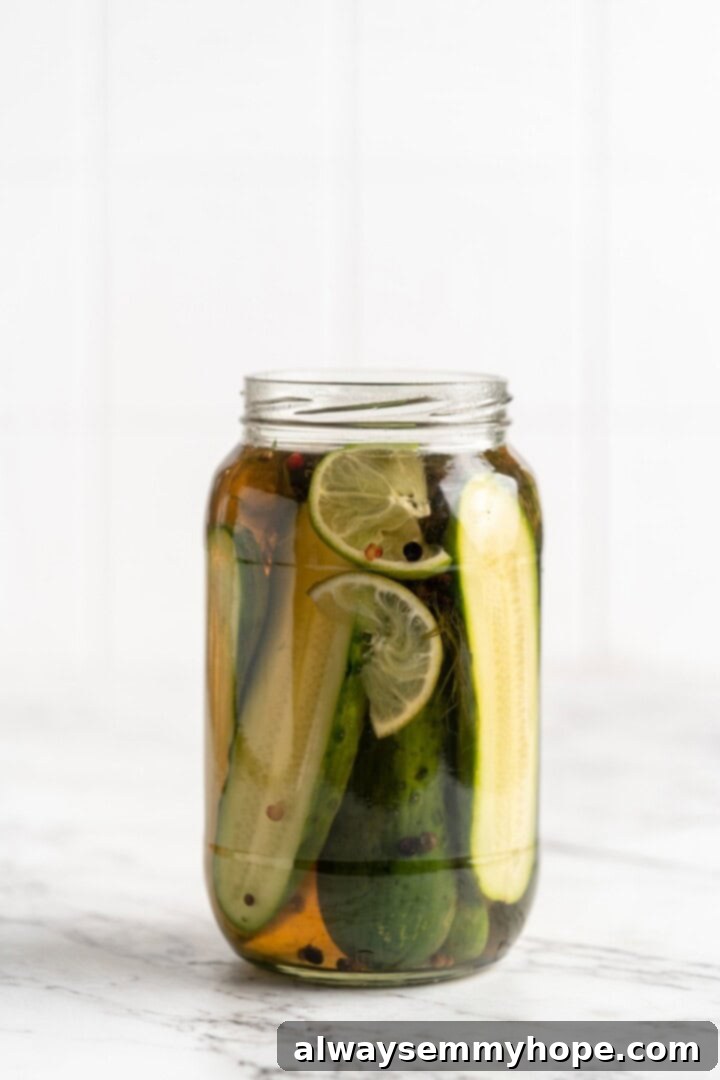 Finished homemade pickles in a jar with lime slices, lid screwed on tight.