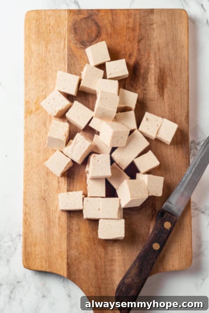 Cut tofu cubes on wooden board with knife