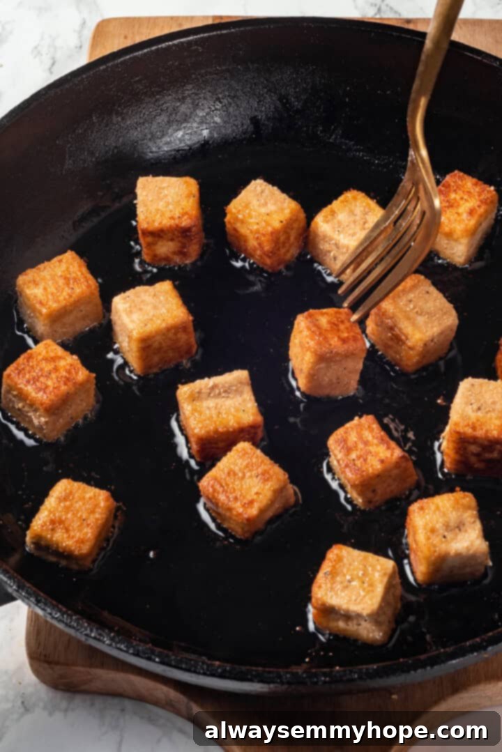 Fork about to pierce piece of tofu frying in skillet