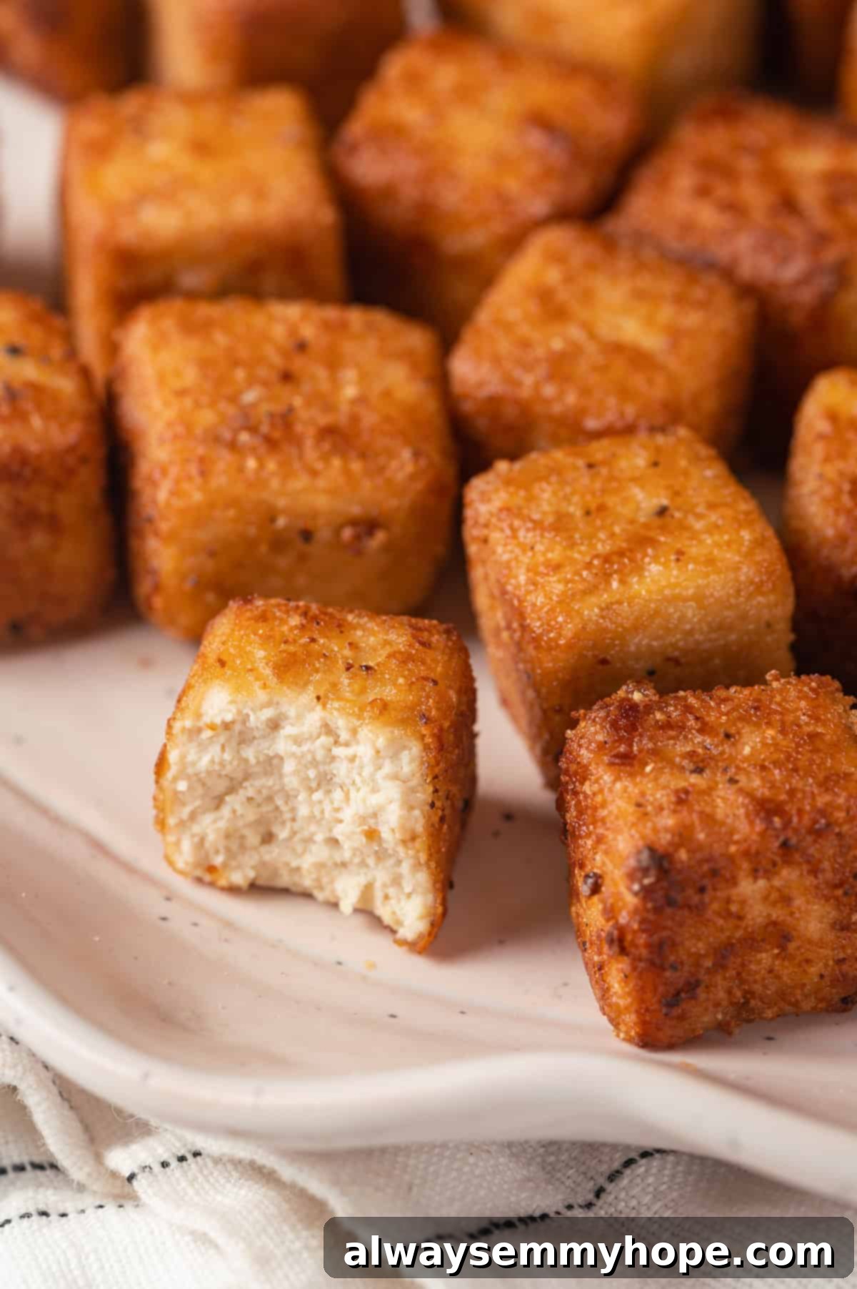 Closeup of fried tofu on plate, with one cube bitten to show soft interior