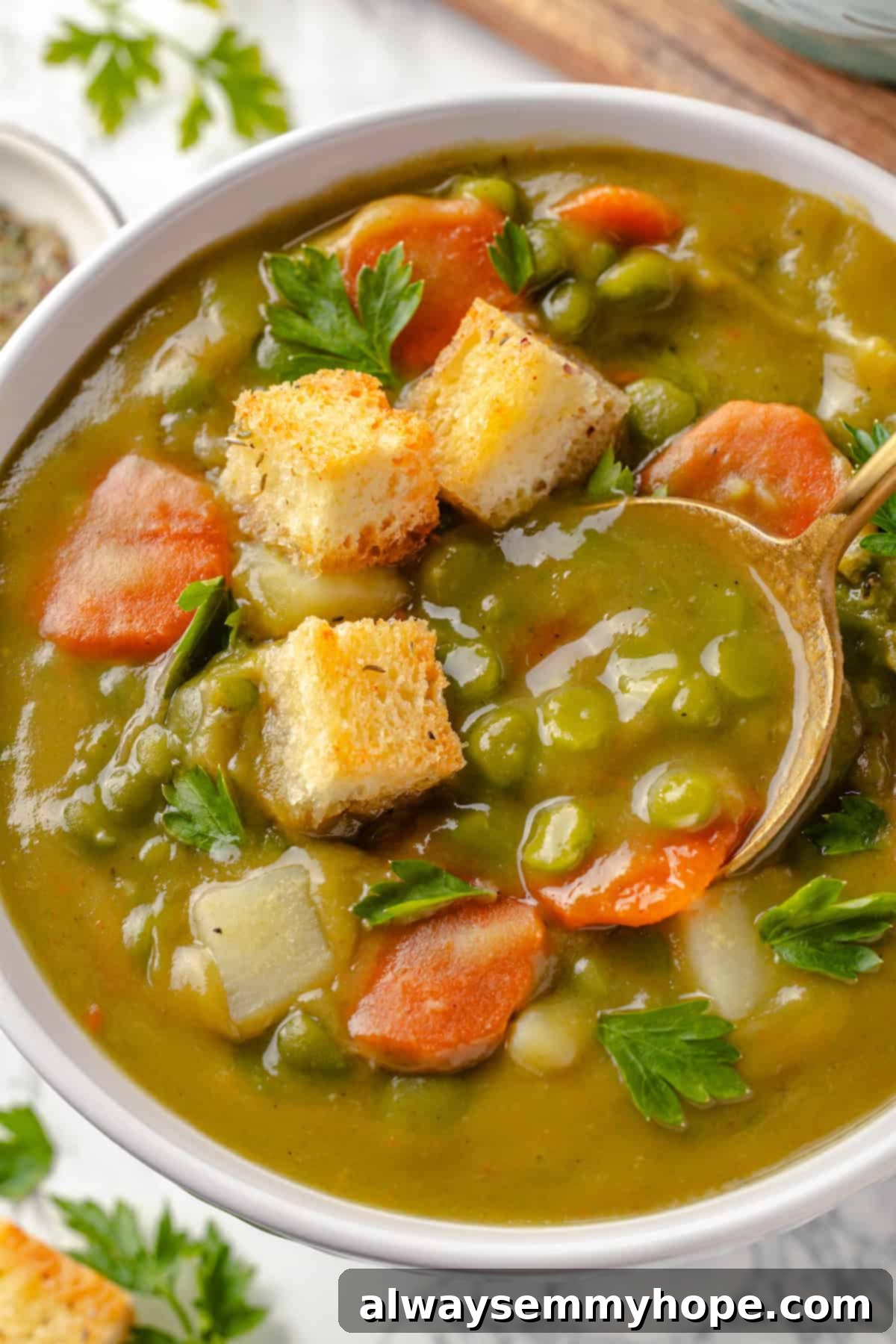 A spoon dipping into a rich, creamy bowl of vegan split pea soup, showcasing its hearty texture and inviting warmth.
