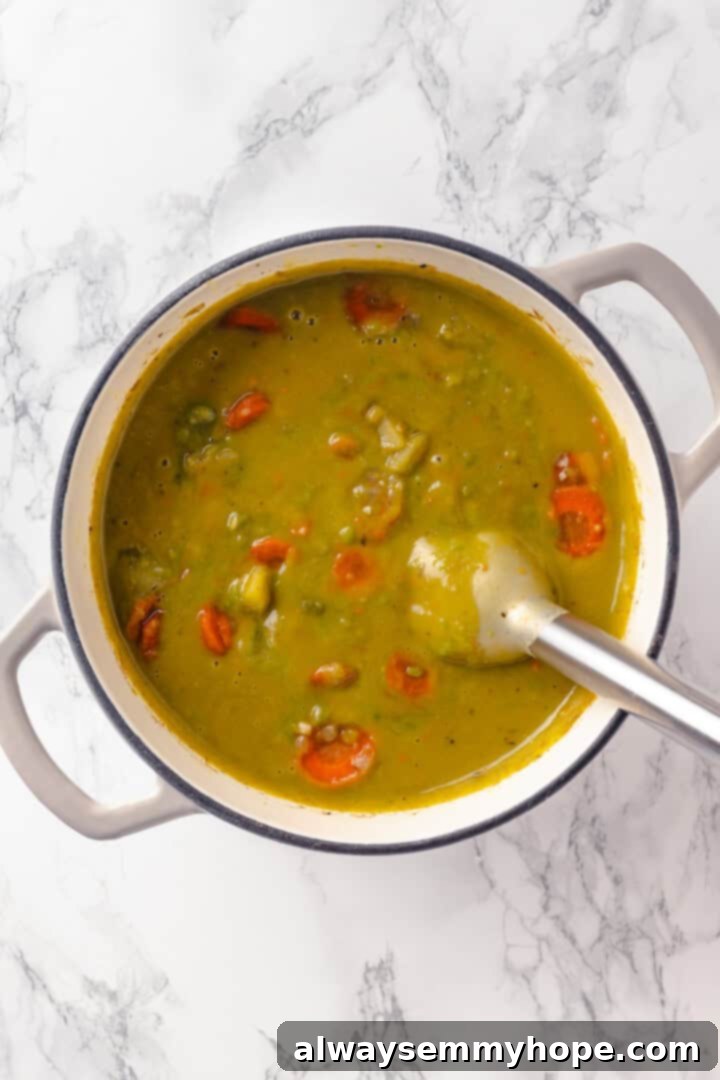 An immersion blender being used to partially blend the vegan split pea soup directly in the pot, creating a creamy yet chunky texture.