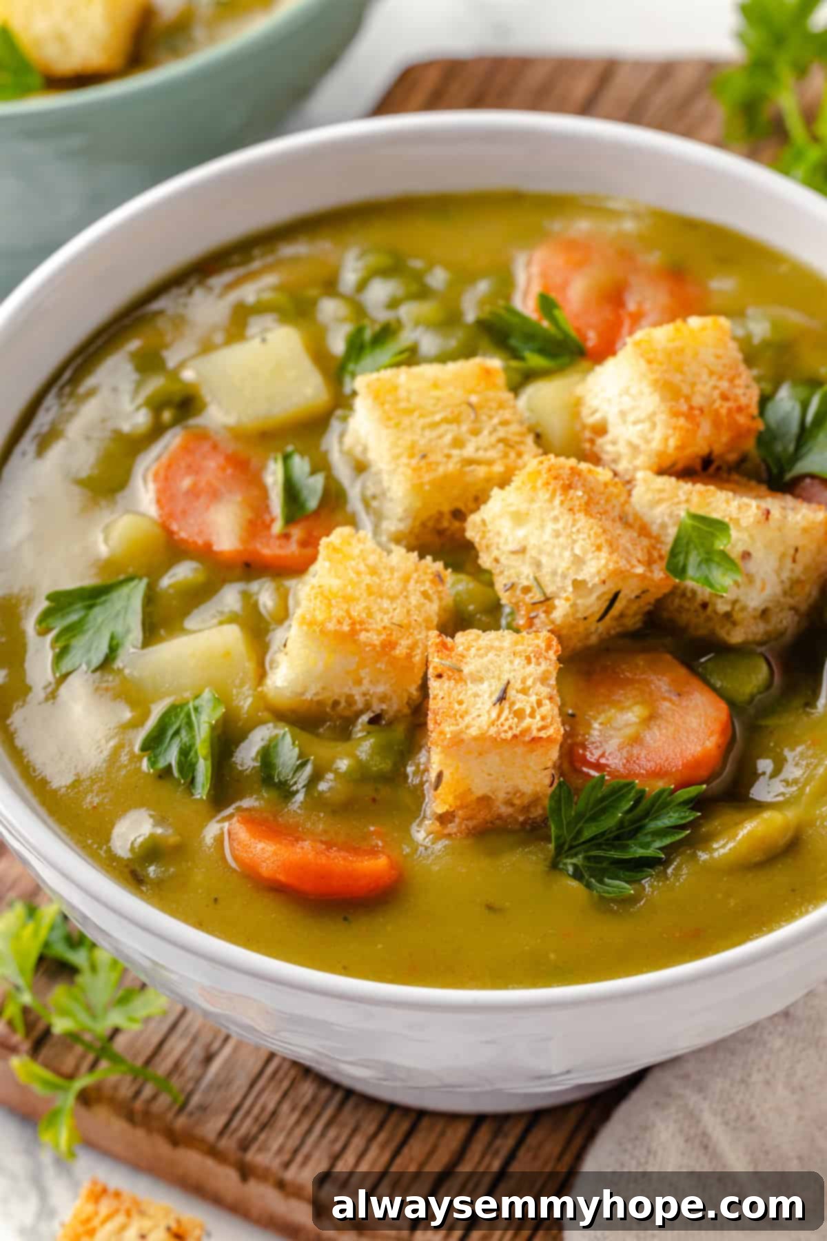 A close-up shot of a bowl of creamy vegan split pea soup, topped with crunchy homemade croutons and a sprinkle of fresh parsley, against a rustic background.