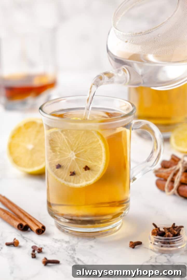 This hot toddy recipe will cure whatever ails you! It's a classic cocktail made with whiskey, lemon juice, and maple syrup to make it vegan. Adding hot water to the hot toddy mixture in a mug, with garnishes nearby