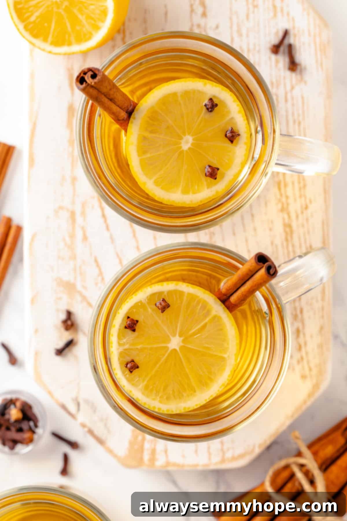 This hot toddy recipe will cure whatever ails you! It's a classic cocktail made with whiskey, lemon juice, and maple syrup to make it vegan. Overhead view of two clear glass mugs of hot toddies with garnishes