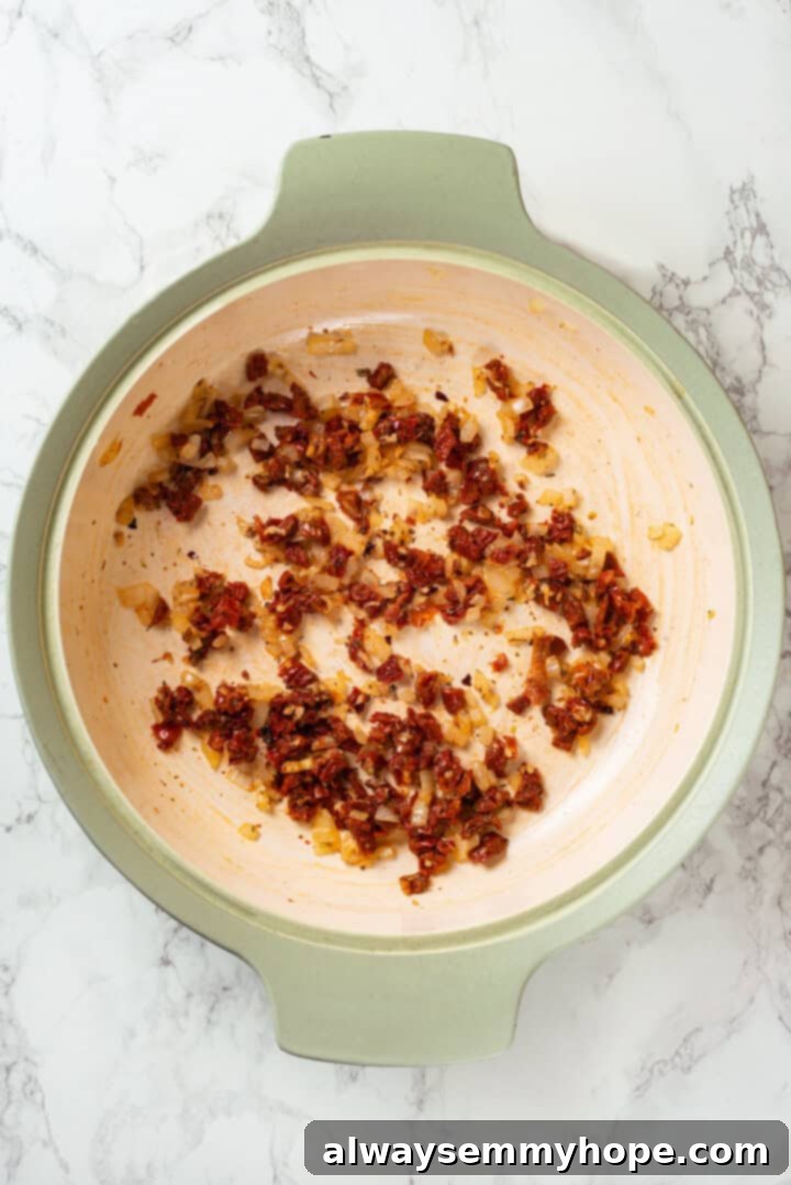 Sautéing finely diced onions, minced garlic, and chopped sun-dried tomatoes in a pan with olive oil, releasing fragrant aromas.