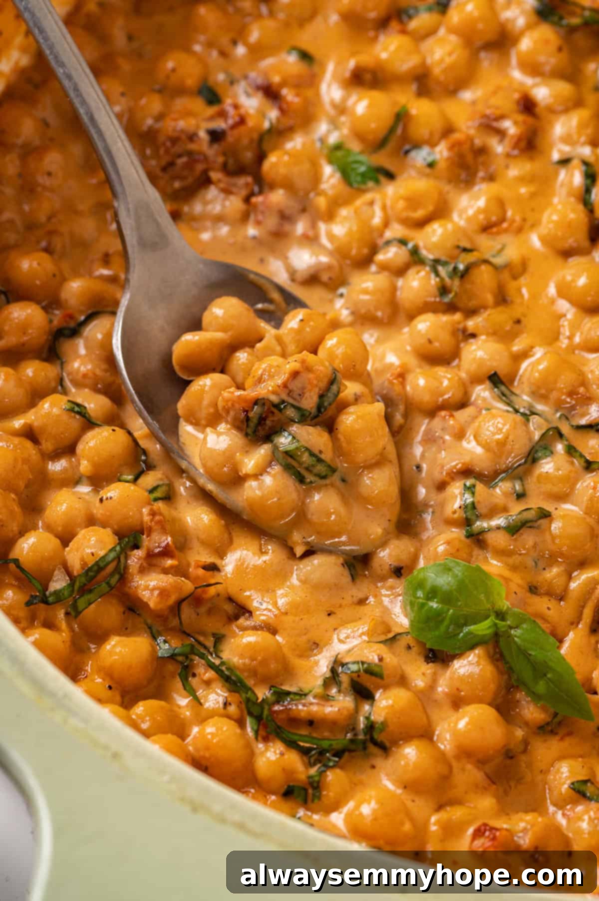 Close-up of a serving spoon in a skillet full of creamy Marry Me Chickpeas, highlighting the rich sauce, sun-dried tomatoes, and fresh basil.