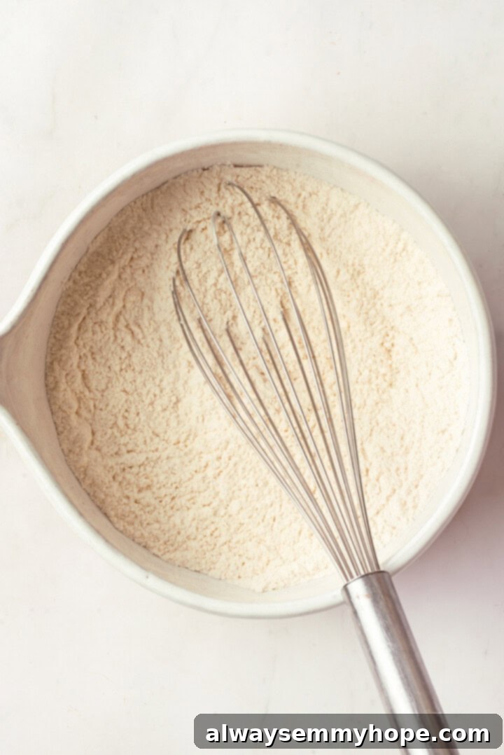 Dry ingredients for peanut butter cookies (flour, baking soda, baking powder, salt) in a mixing bowl with a whisk
