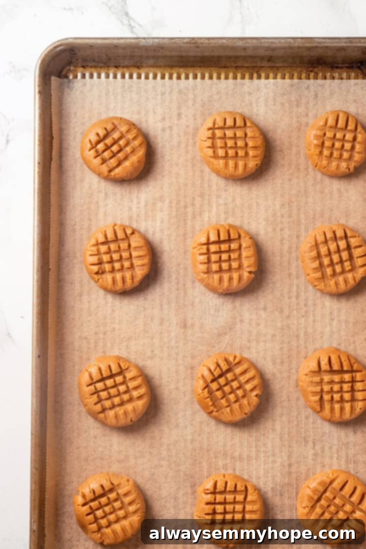 Overhead view of vegan peanut butter cookie dough balls on a baking sheet with the classic criss-cross fork pattern pressed into them