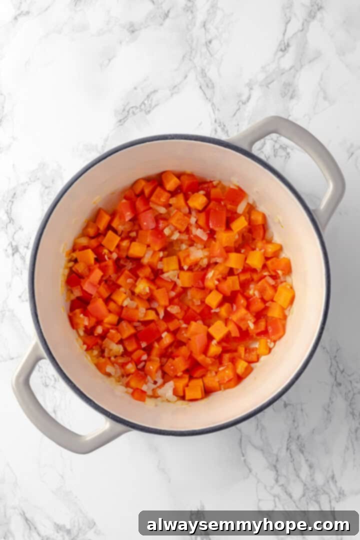 Watch the vegetables soften in the pot, building the flavorful base for your mega cheesy vegan lasagna soup. Overhead view of softened onions, garlic, carrots, and bell peppers gently cooking in olive oil within a large pot.