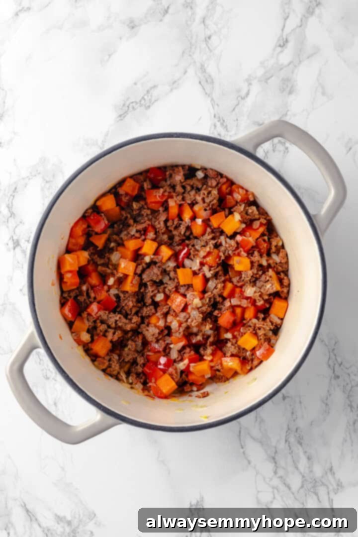 Add the vegan sausage to the pot, browning it with the vegetables to create a rich, savory base for your vegan lasagna soup. Overhead view of crumbled vegan sausage browning alongside the softened vegetables in the pot, releasing savory aromas.