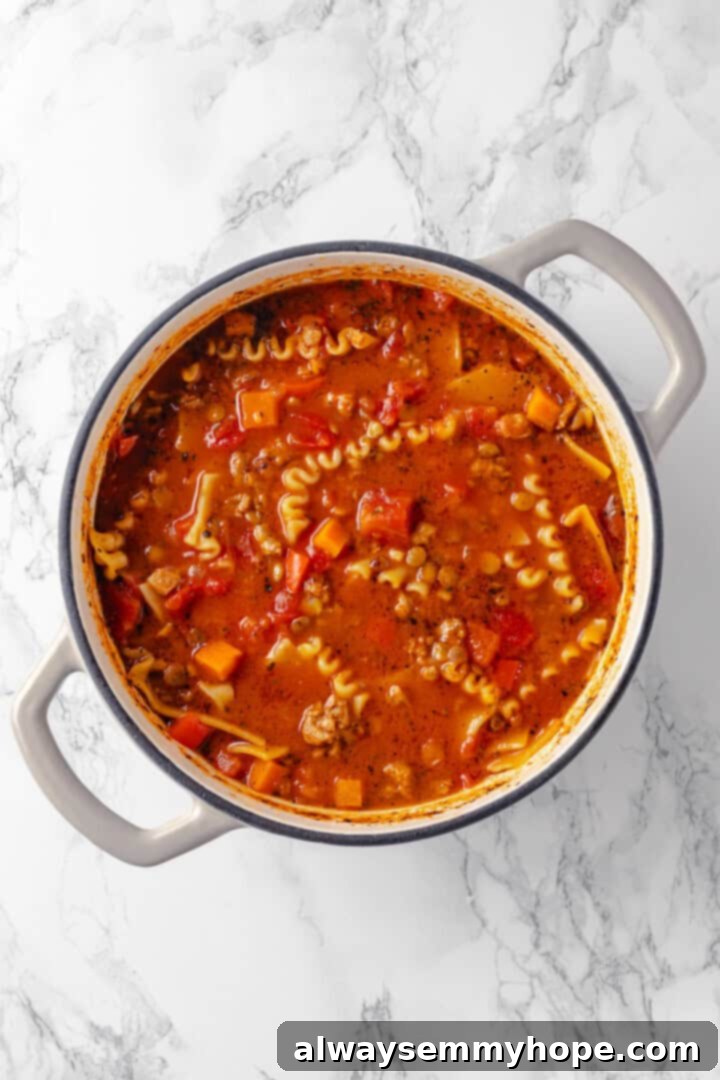 Watch the broken lasagna noodles cook to perfection within the savory soup, creating the iconic texture of lasagna. Overhead view of broken lasagna noodles cooking gently within the simmering vegan lasagna soup, absorbing all the rich flavors.