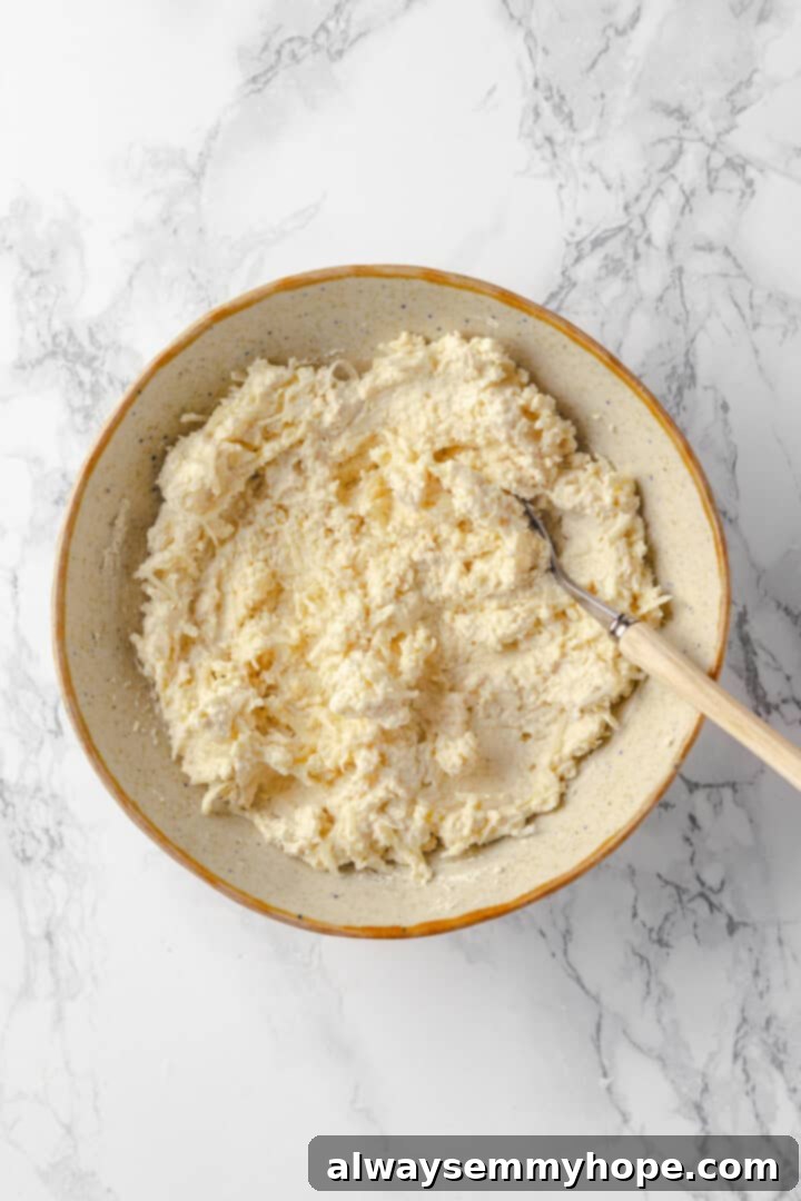 Mix the creamy vegan cheese topping while the soup simmers, ensuring it's ready for a decadent garnish. Overhead view of the creamy vegan cheese topping mixture (ricotta, mozzarella, parmesan) in a bowl with a spoon, ready for serving.
