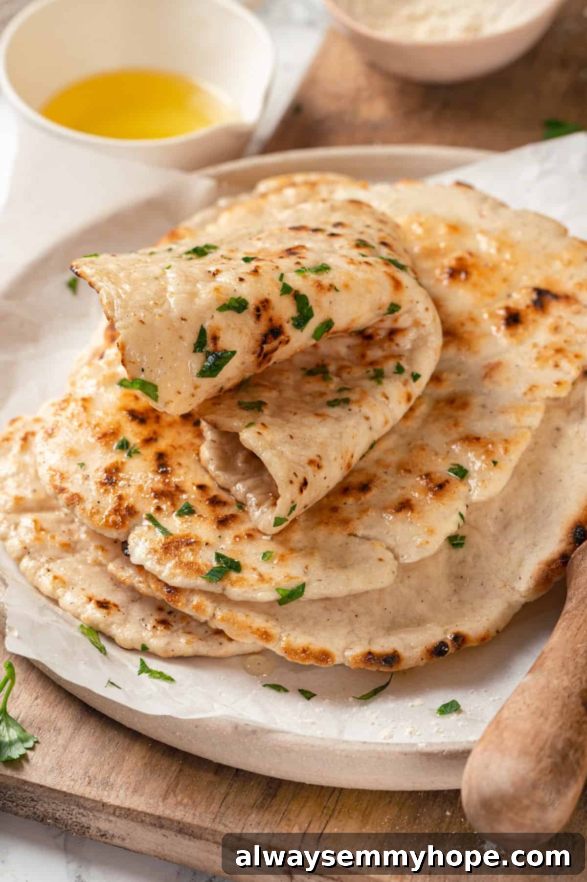 This easy gluten-free naan recipe has the chewy texture and slightly charred bits that make naan so irresistible, but without the wheat! Stack of freshly made gluten-free naan on a rustic plate, showing its soft, chewy texture and slight charring.