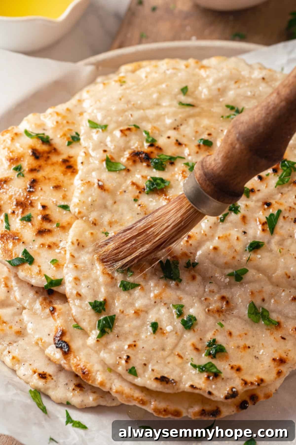 This easy gluten-free naan recipe has the chewy texture and slightly charred bits that make naan so irresistible, but without the wheat! A hand brushing melted butter or oil onto a warm piece of gluten-free naan, adding shine and flavor.