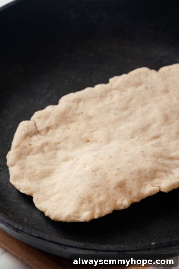 This easy gluten-free naan recipe has the chewy texture and slightly charred bits that make naan so irresistible, but without the wheat! A piece of gluten-free naan dough placed into a hot cast iron skillet, ready to cook and puff up.