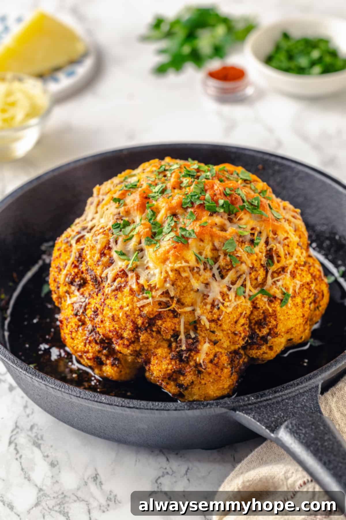 A close-up, appetizing view of a whole roasted cauliflower, beautifully cooked to a golden brown in a cast iron skillet.