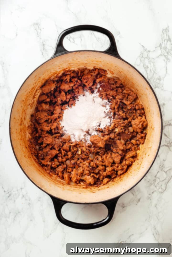 All-purpose flour being sprinkled into a pot of browned vegan sausage mixture to create a roux.