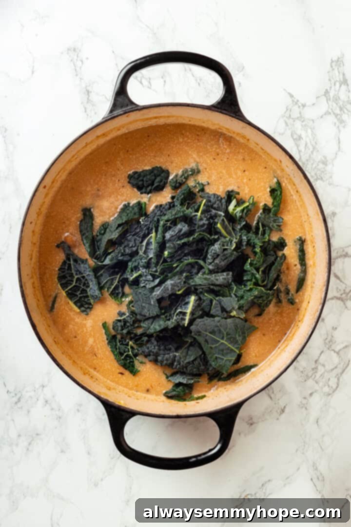 Zuppa toscana is creamy and hearty with tender potatoes and kale, and this vegan version is just as tasty as the Olive Garden original! Chopped kale added to pot of creamy soup.