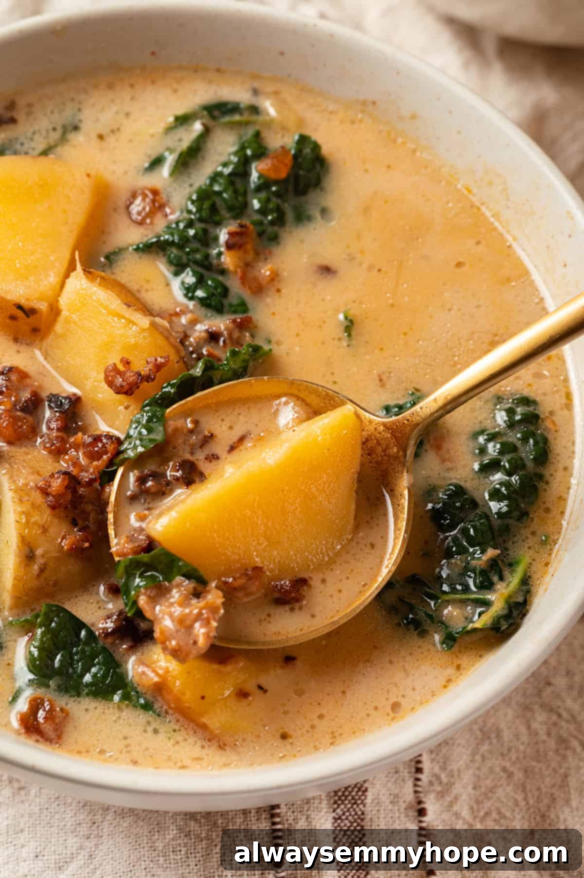 Zuppa toscana is creamy and hearty with tender potatoes and kale, and this vegan version is just as tasty as the Olive Garden original! Spoonful of creamy vegan zuppa toscana being lifted from a bowl.