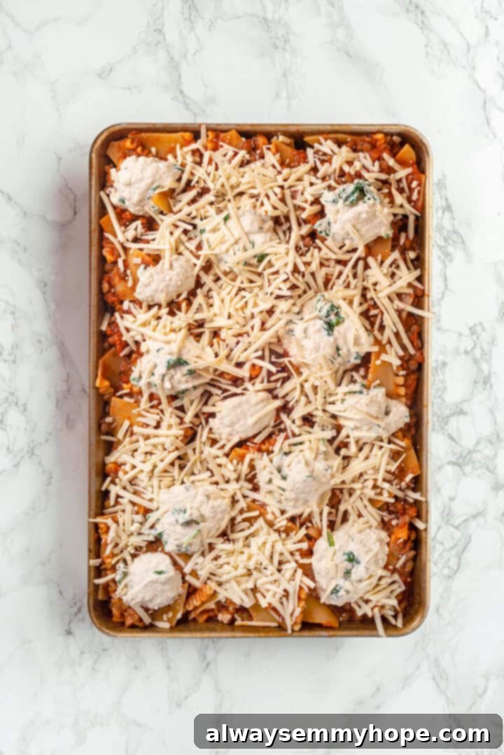 This vegan sheet pan lasagna recipe is a different way to enjoy all that cheesy pasta goodness—easier, quicker, and more crispy edges! Overhead view of a sheet pan filled with assembled vegan lasagna layers, ready for baking.