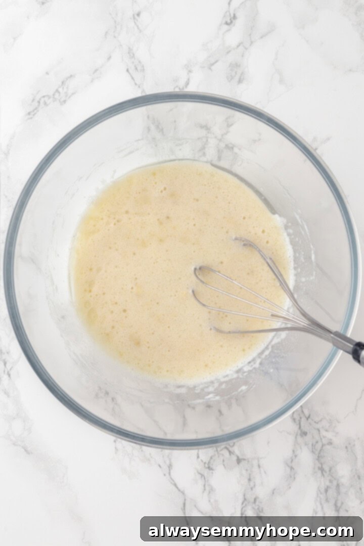 Wet ingredients including mashed banana, plant milk, sugar, vanilla, and oil in a mixing bowl with a whisk