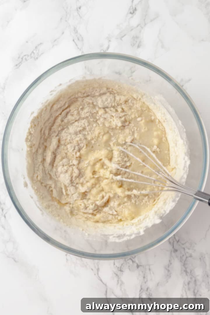 Adding dry ingredients to wet ingredients in a bowl, with a whisk gently combining the banana pancake batter