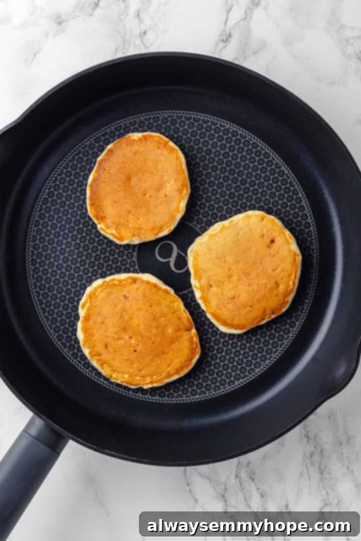 Overhead view of several golden brown vegan banana pancakes cooking in a skillet after being flipped
