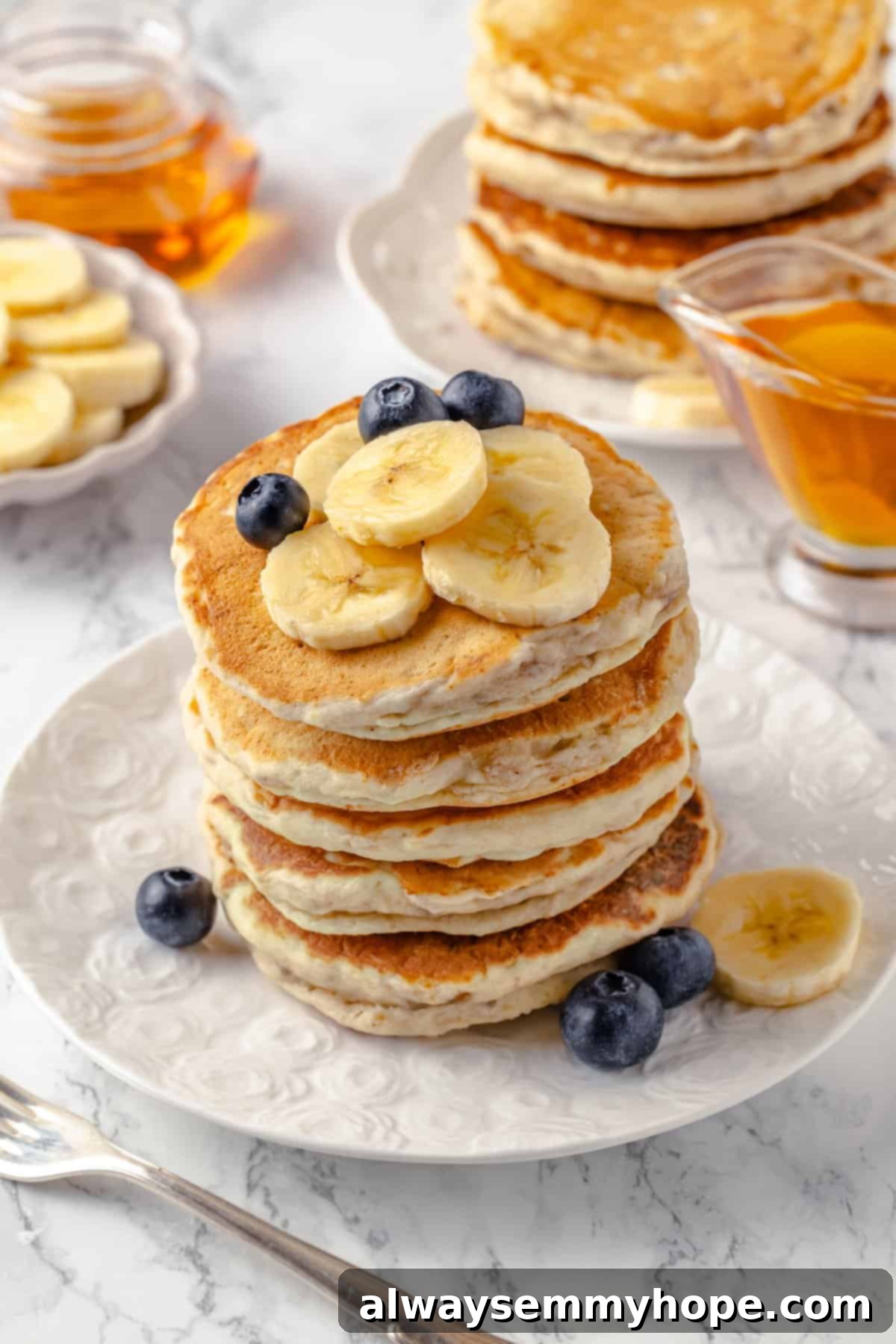 A beautifully stacked plate of fluffy banana pancakes, garnished with fresh raspberries, blueberries, and a mint sprig