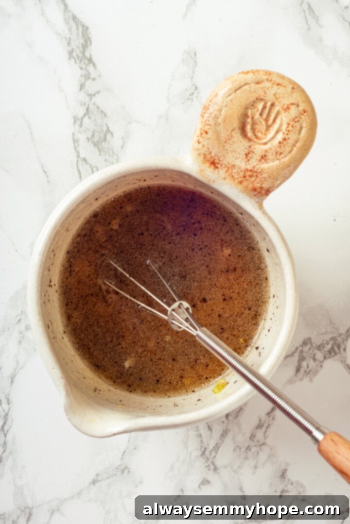 Overhead view of a small bowl containing the lemon dressing, with a whisk resting inside, showing its emulsified texture.