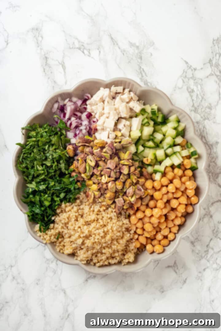 Overhead view of all the prepared salad ingredients, including quinoa, chickpeas, diced vegetables, and herbs, ready for assembly in a large bowl.