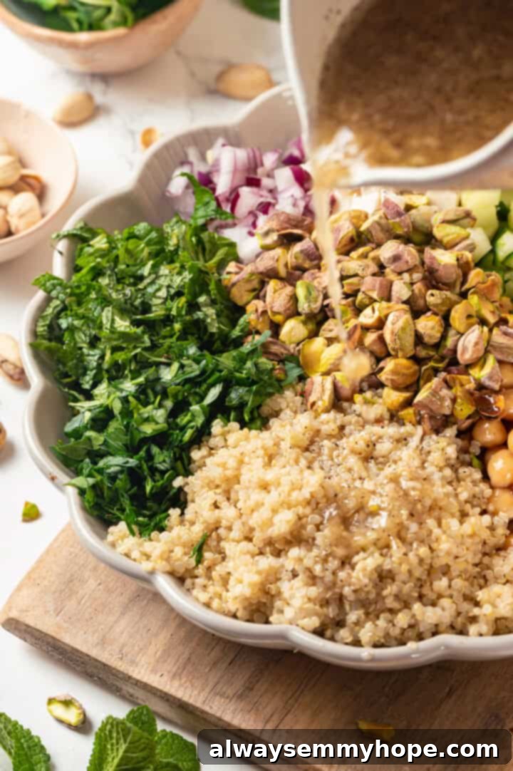 A stream of zesty lemon dressing being poured over the assembled vegan Jennifer Aniston salad in a large mixing bowl.