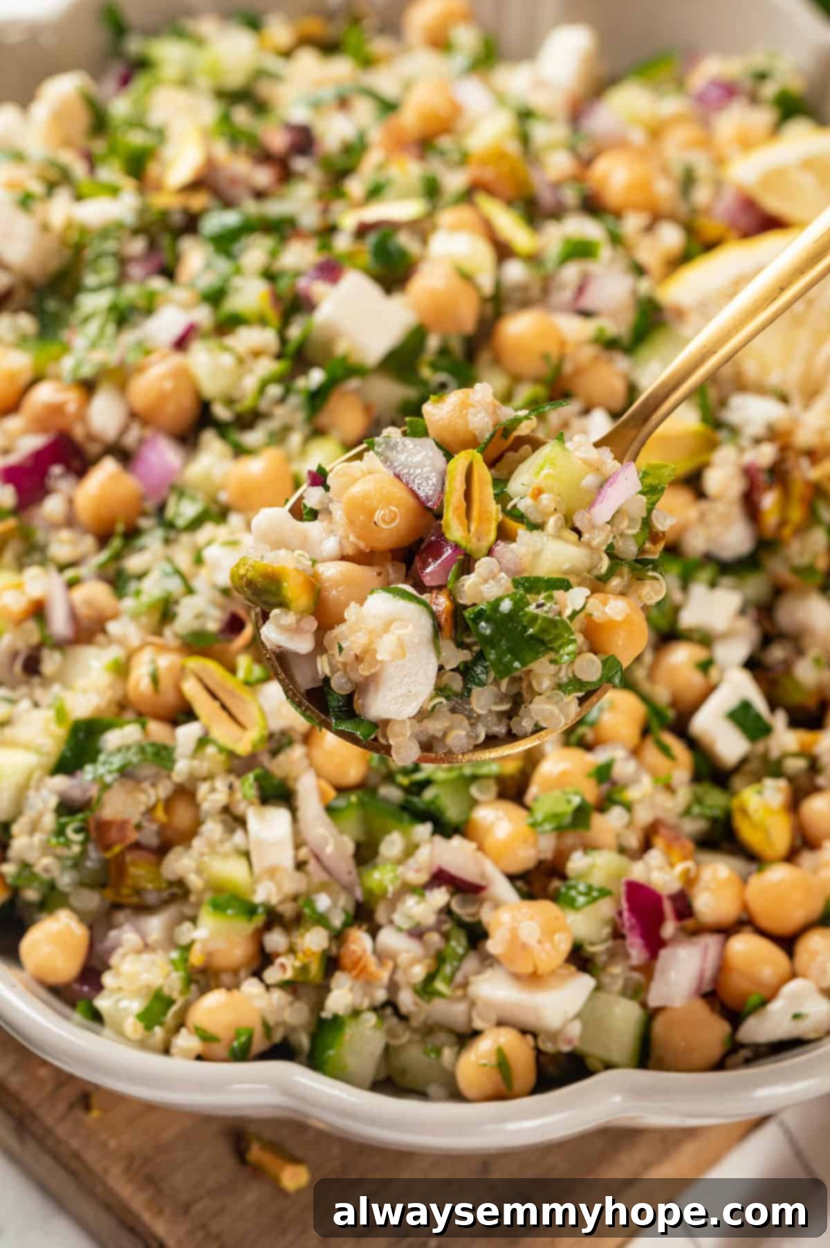 A spoonful of vegan Jennifer Aniston salad held elegantly over a serving bowl, showcasing the colorful ingredients.