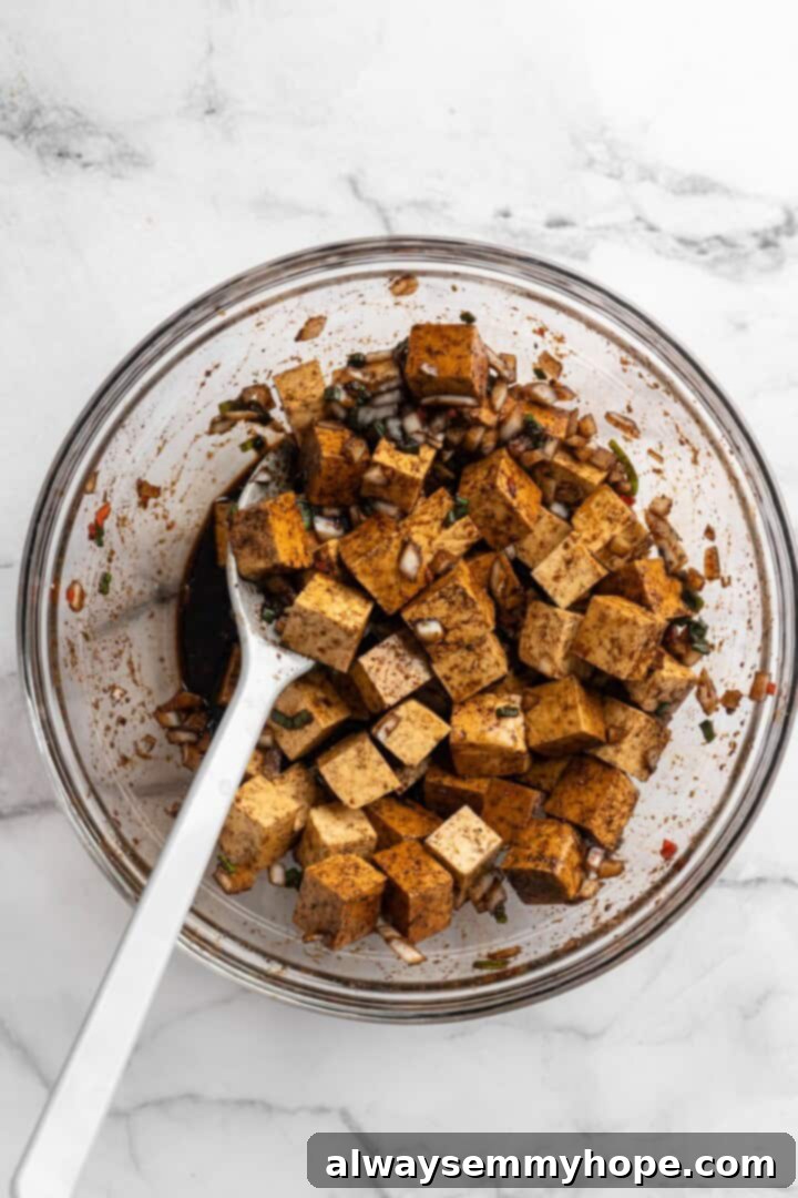 This brown stew tofu recipe is a flavourful, hearty dinner inspired by traditional Jamaican cooking—but with a vegan twist! Stirring tofu in a rich, dark marinade in a bowl
