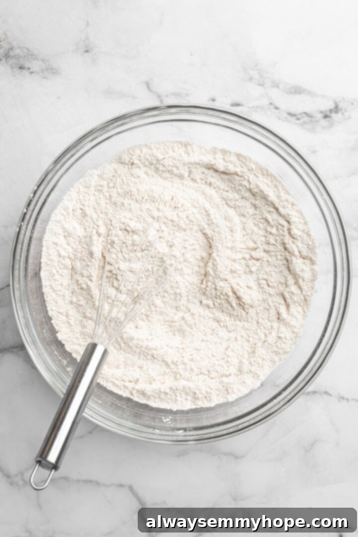 Dry dough ingredients in bowl with whisk, including flour, turmeric, salt, and sugar