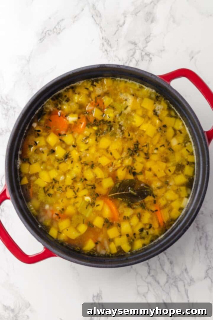 Overhead view of vegetables simmering in vegetable broth with miso paste and a bay leaf.