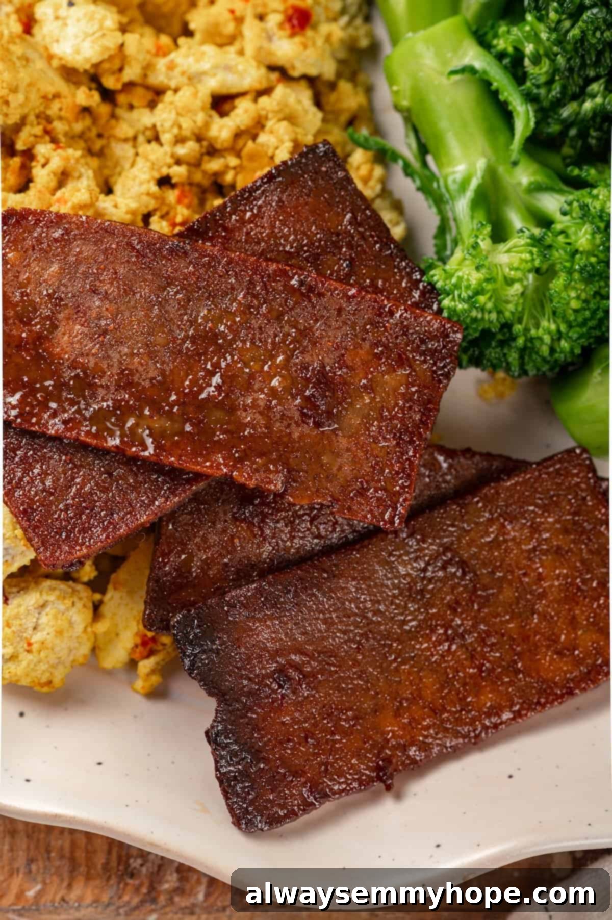 Complete Vegan Breakfast with Tofu Bacon A delectable vegan breakfast spread featuring a plate with golden tofu bacon, a fluffy vegan scramble, and vibrant green broccoli, all ready to be savored.