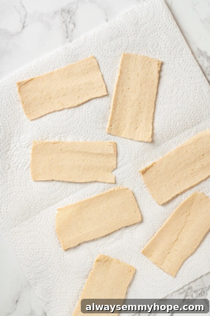 Slicing and Drying Tofu for Bacon Thinly sliced firm tofu arranged on paper towels to absorb excess moisture, a crucial step for crispy tofu bacon.