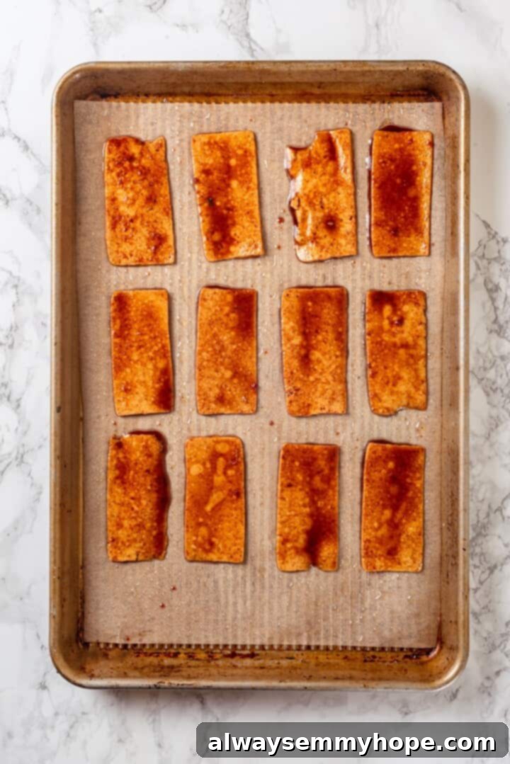 Ready to Bake Vegan Tofu Bacon Thinly sliced, marinated tofu bacon strips neatly arranged on a parchment-lined baking sheet, ready for oven baking.