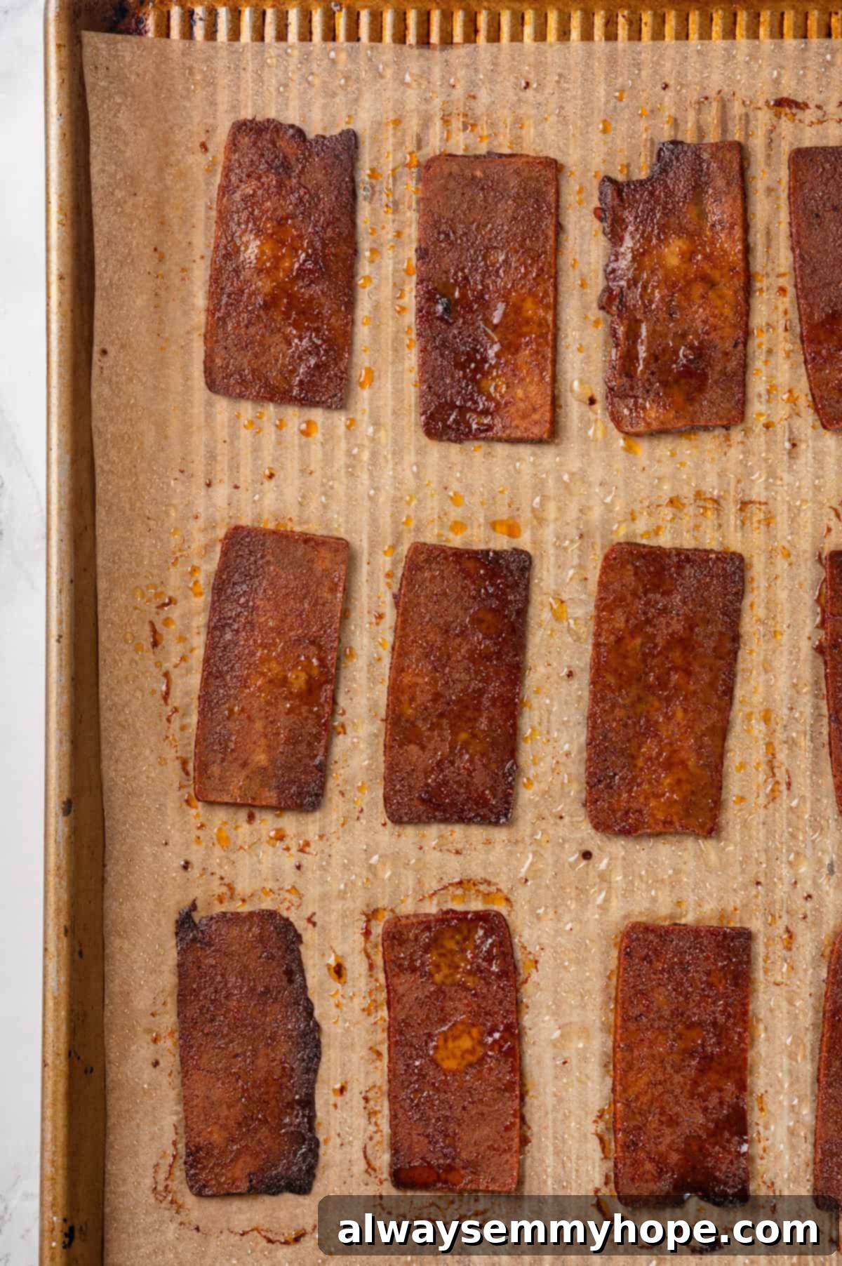 Freshly Baked Crispy Tofu Bacon A close-up overhead view of golden-brown, crispy tofu bacon strips arranged perfectly on a parchment-lined baking pan, freshly baked.