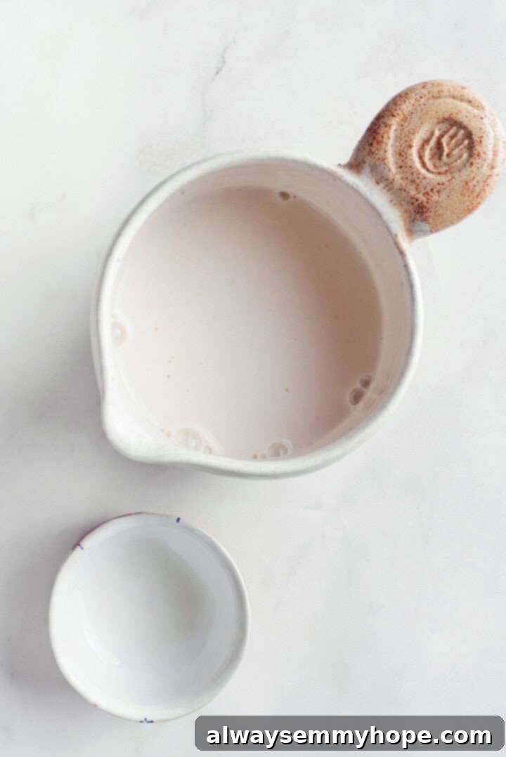 Prepping vegan buttermilk for the recipe. Two small bowls, one with plant milk and the other with apple cider vinegar, ready to be combined to create vegan buttermilk for the cake batter.