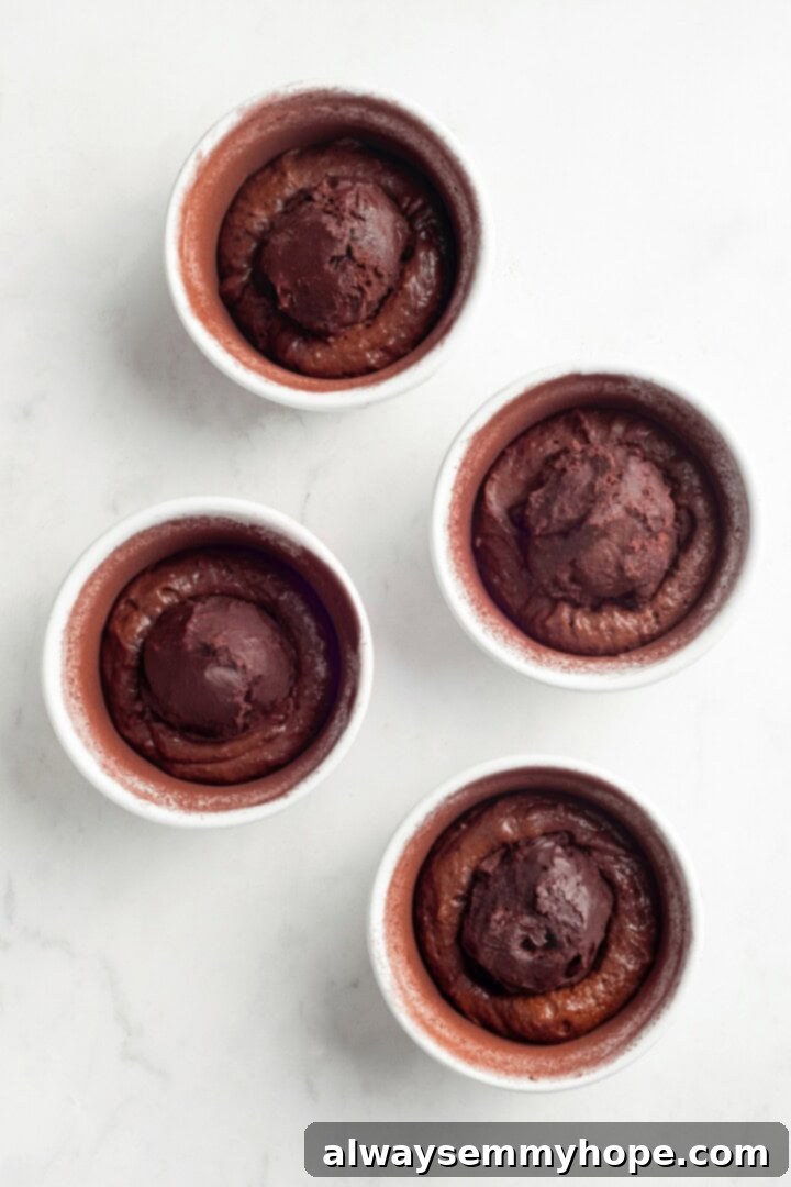 Adding the ganache to the ramekins with batter. Greased ramekins with a layer of vegan chocolate cake batter, topped with a scoop of firm chilled ganache, ready for the final layer of batter.