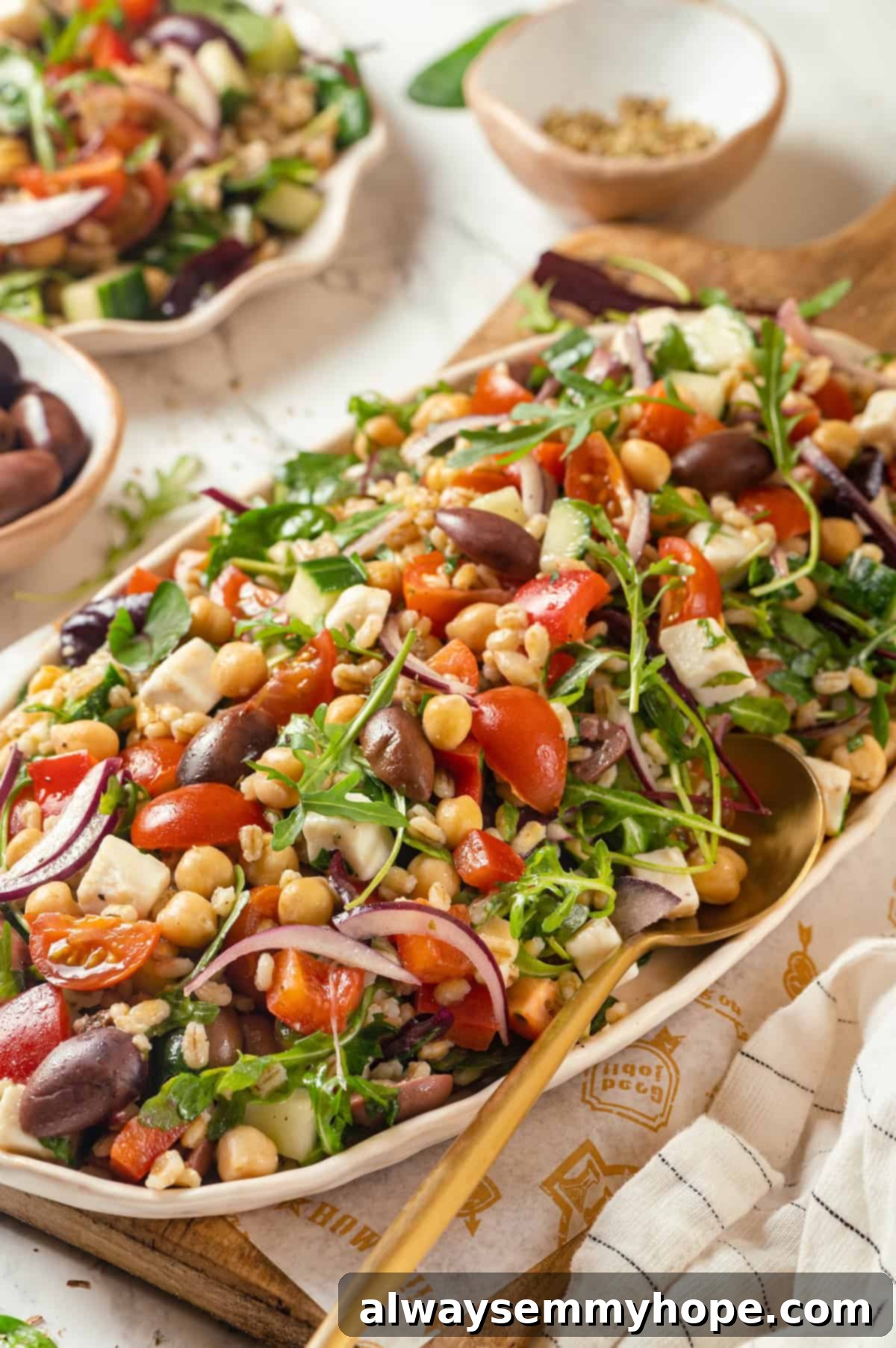 This farro salad is hearty and satisfying, with bright and bold Greek flavours to make it delicious. It might just be the perfect lunch! Hearty platter of vibrant Greek farro salad with chickpeas, cucumbers, tomatoes, and vegan feta, ready for serving