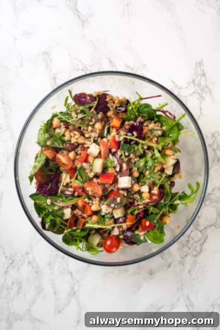 This farro salad is hearty and satisfying, with bright and bold Greek flavours to make it delicious. It might just be the perfect lunch! Overhead view of perfectly dressed Greek farro salad in a clear glass bowl